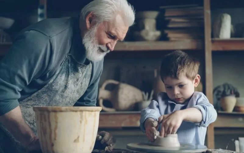 A grandfather teaches his grandson pottery in a creative pottery workshop setting.