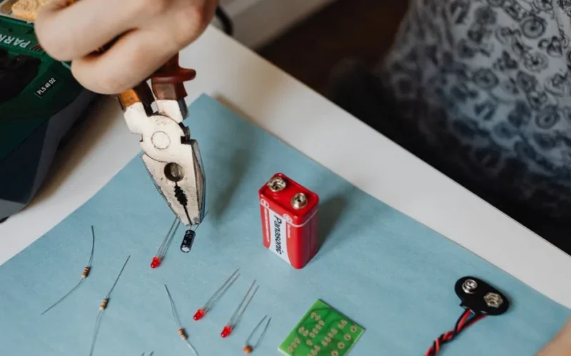 Close-up of electronics repair using pliers with resistors and battery.