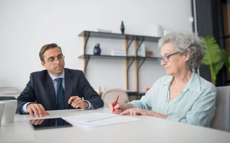 Elderly woman signing paperwork in modern office with consultant.