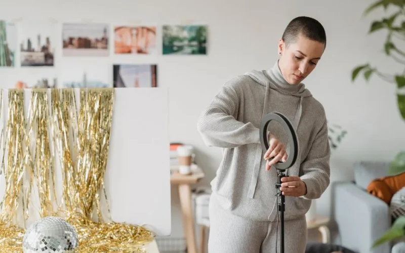 Young focused female in hoodie installing professional lamp against frippery and decorative ball in house room