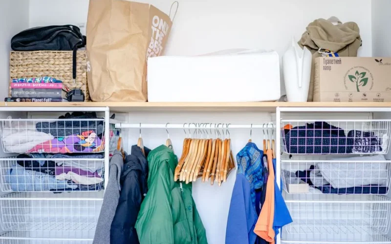 A minimalist open wardrobe featuring modern clothing, hangers, and storage baskets.
