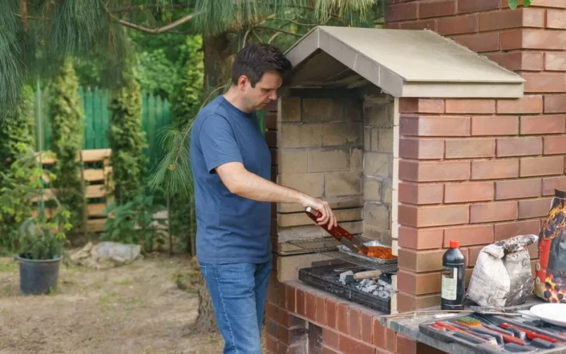 A man grills meat on a brick barbecue in the garden, showcasing outdoor cooking and leisure activity.