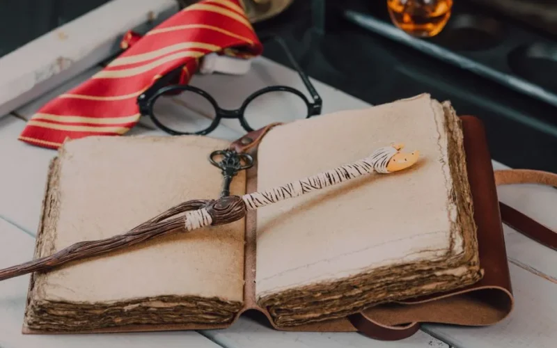 Explore this enchanting close-up of wizard-themed items including a spell book, wand, and Gryffindor tie.