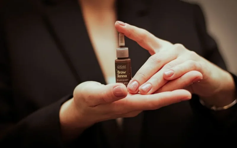 Elegant close-up of a woman holding Brow Henna cosmetic product, showcasing nail polish and packaging.