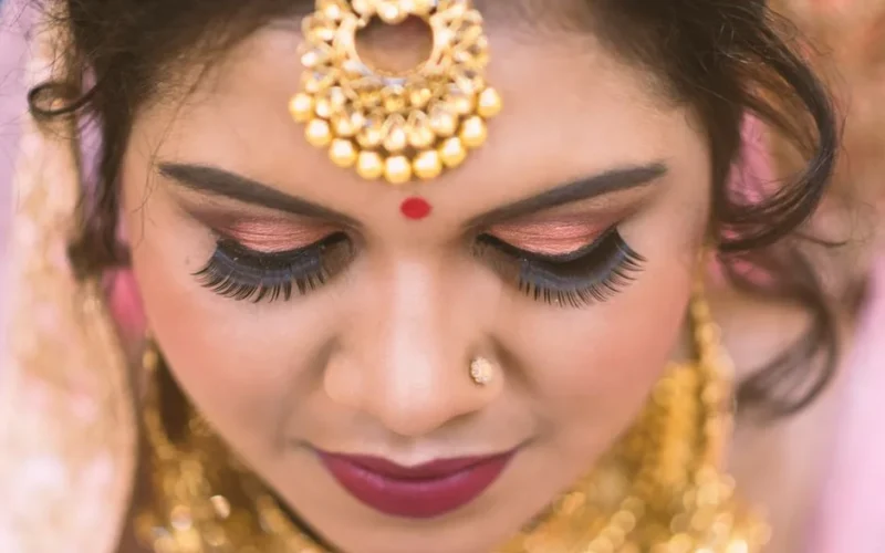 Close-up view of an Indian woman adorned with traditional bridal makeup and gold jewelry accentuating her features.