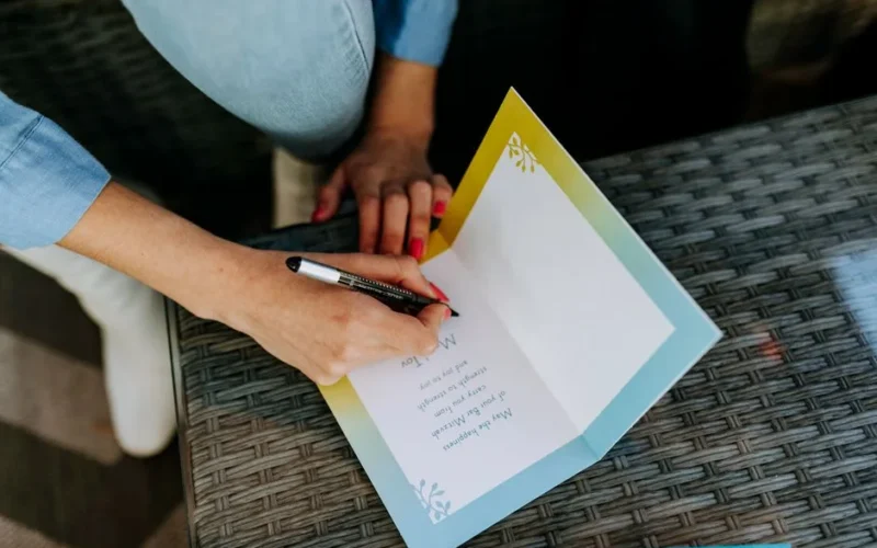 Top view of a person writing a message in a greeting card on a table.