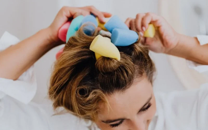 Close-up of a woman using colorful foam rollers to style her hair indoors.