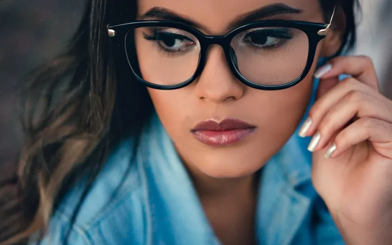 Stylish close-up portrait of a young woman wearing eyeglasses and denim shirt.
