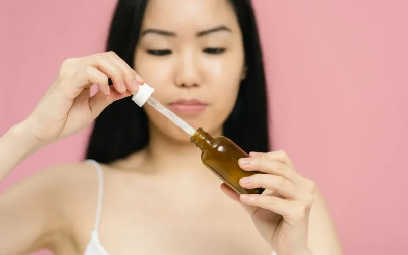 Close-up of a woman holding a serum bottle with a dropper, focusing on skincare.