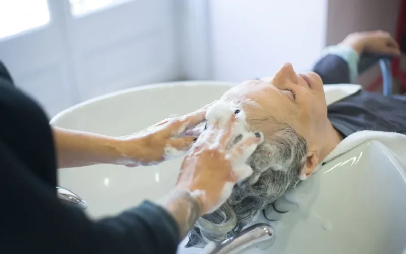Close-up of senior woman getting hair washed with foam at salon sink, enjoying the pampering session.