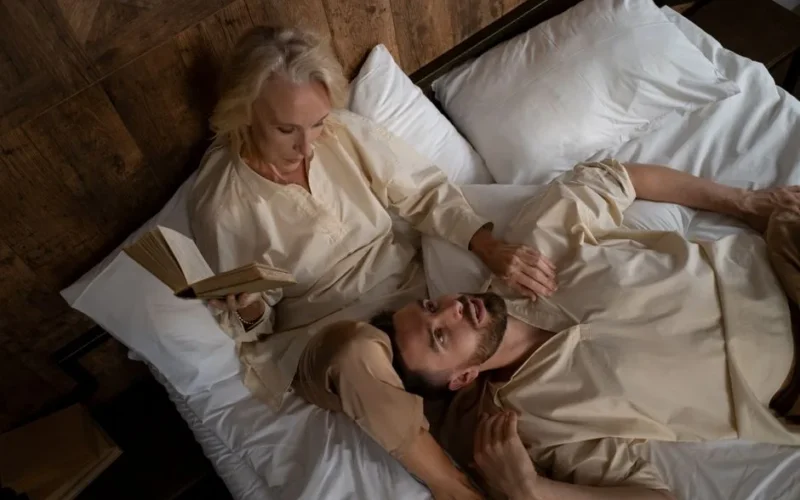 A couple in bed wearing pajamas, relaxing and reading together, conveying warmth and intimacy.