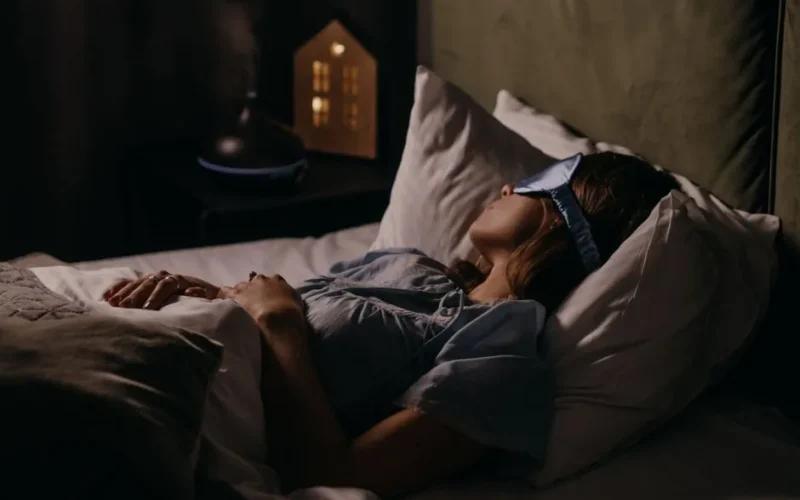 A woman peacefully sleeping with an eye mask in a dimly lit bedroom, capturing a serene bedtime atmosphere.