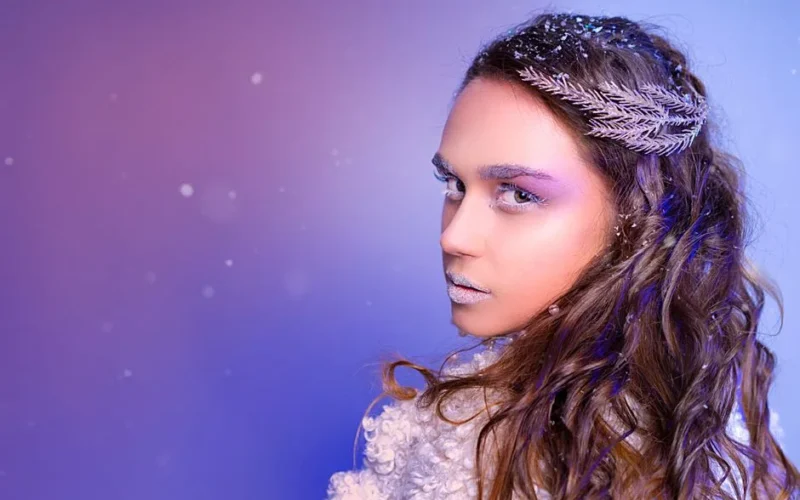 A captivating winter-themed portrait of a woman with snowflakes and icy makeup against a purple background.