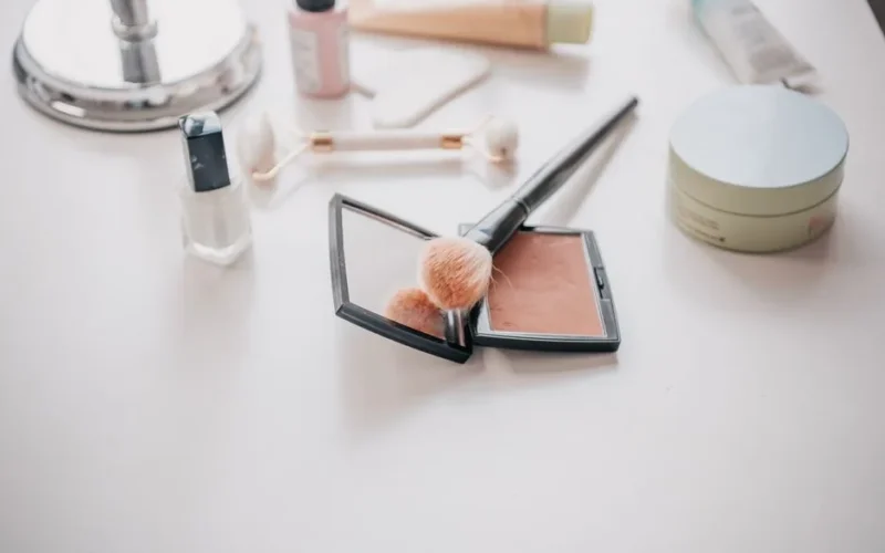 Image of makeup essentials including brushes, compacts, and creams on a vanity table.