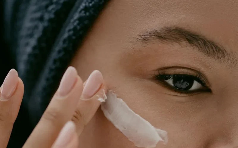 Extreme close-up of a woman applying cream to her cheek for healthy skin care.