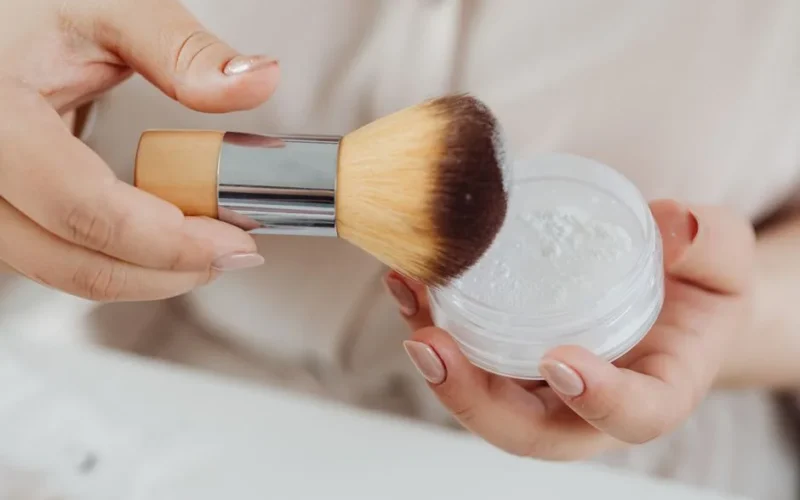 Close-up view of a hand applying face powder with a makeup brush, perfect for beauty and lifestyle concepts.