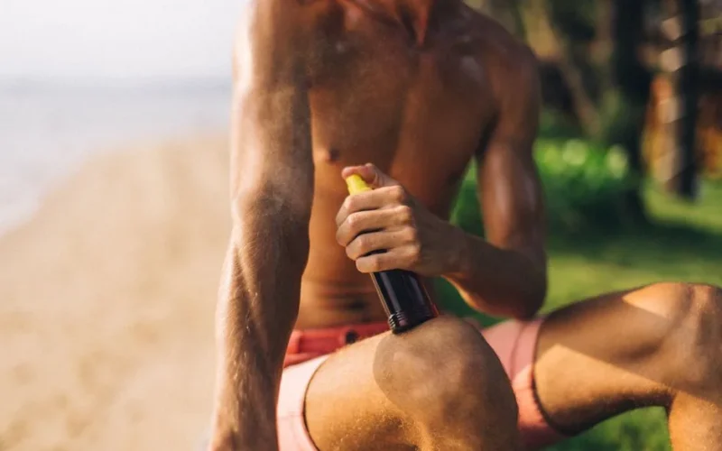 Close-up of a man applying tanning spray on a sunny beach day.