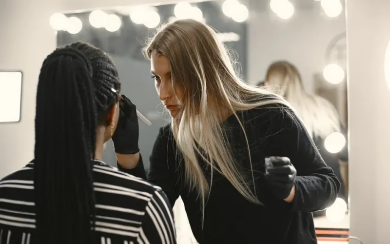 Makeup artist skillfully applies makeup on client in a well-lit studio with mirror lights.