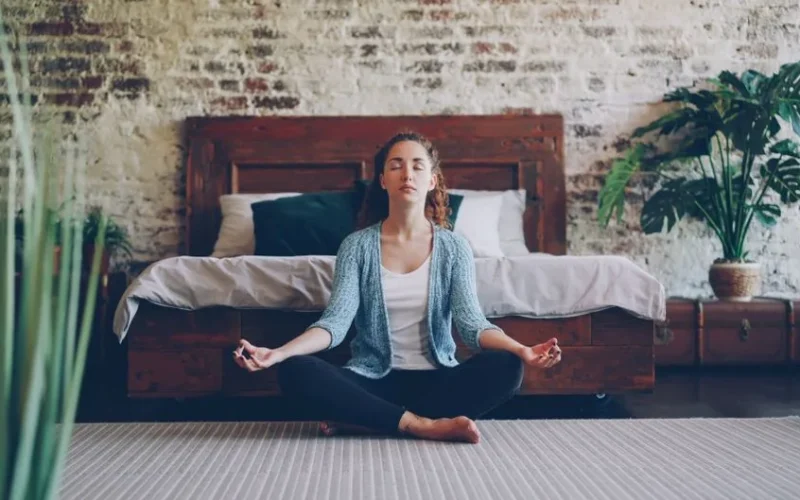 Tranquil scene of a woman meditating in a stylish bedroom with natural decor.