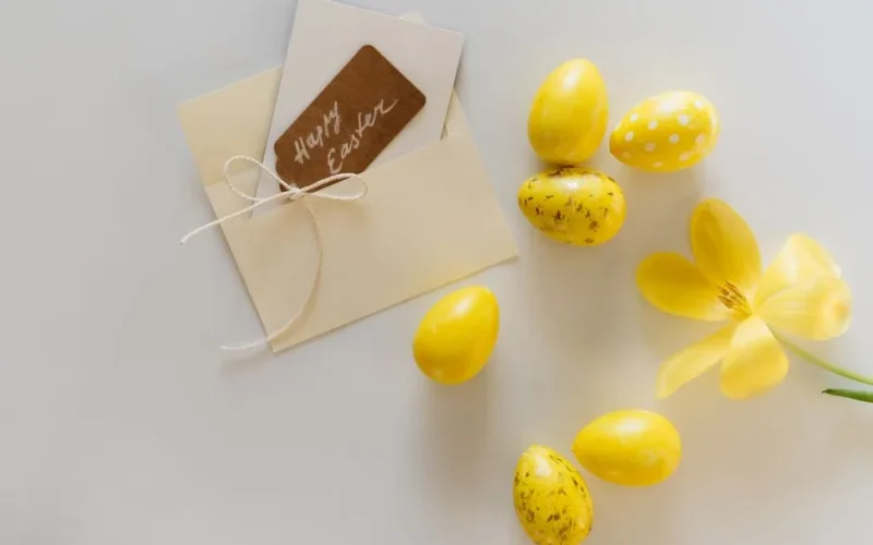 A charming Easter setup with yellow eggs, flower, and a greeting card on a white surface.