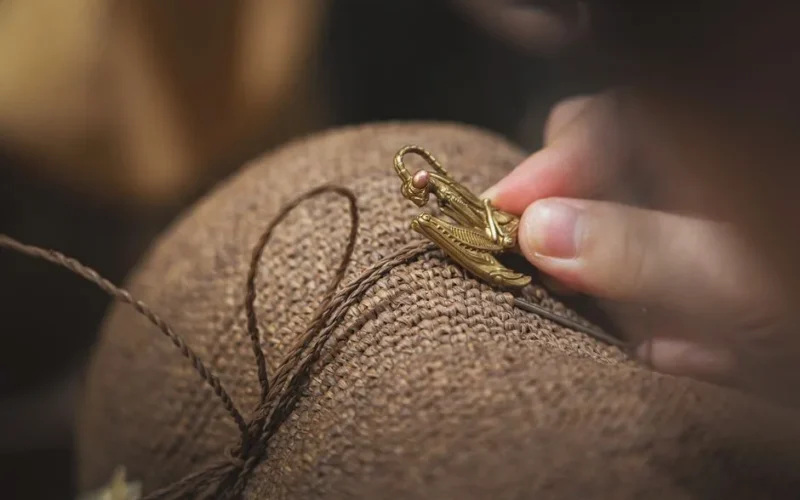A hand decorates a straw hat with a golden insect-shaped brooch, showcasing detailed craftsmanship.