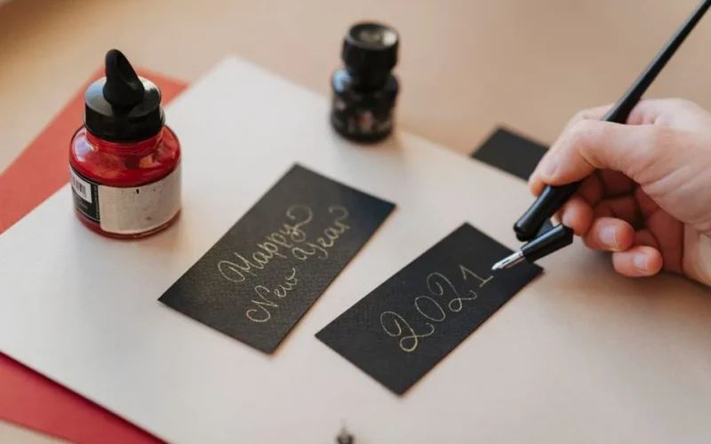 A hand writes 'Happy New Year 2021' in calligraphy with a fountain pen.