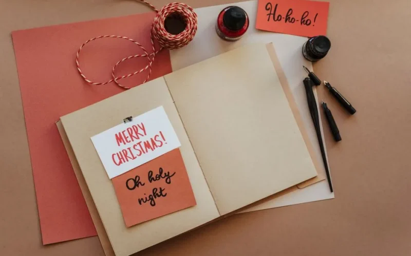 A warm and cozy still life of Christmas card crafting materials on a brown background.