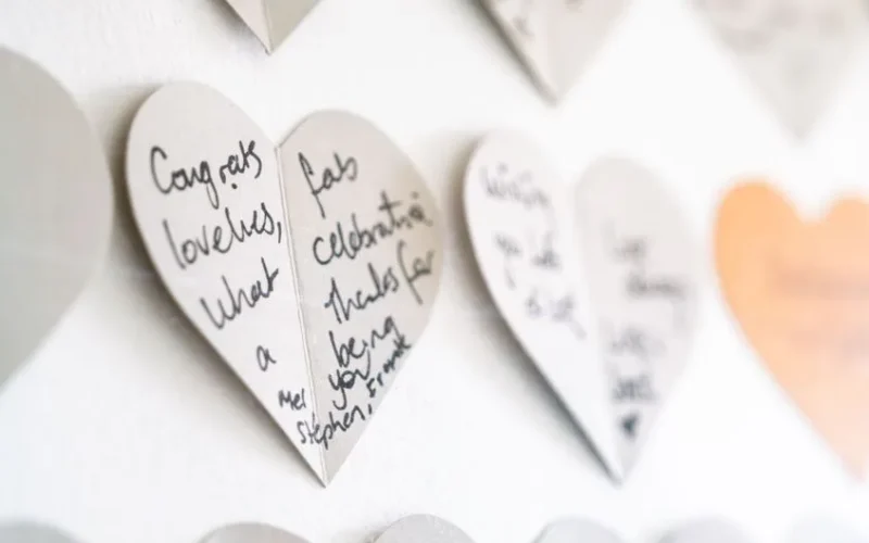 Close-up view of heart-shaped cards with handwritten congratulatory messages on a wall.