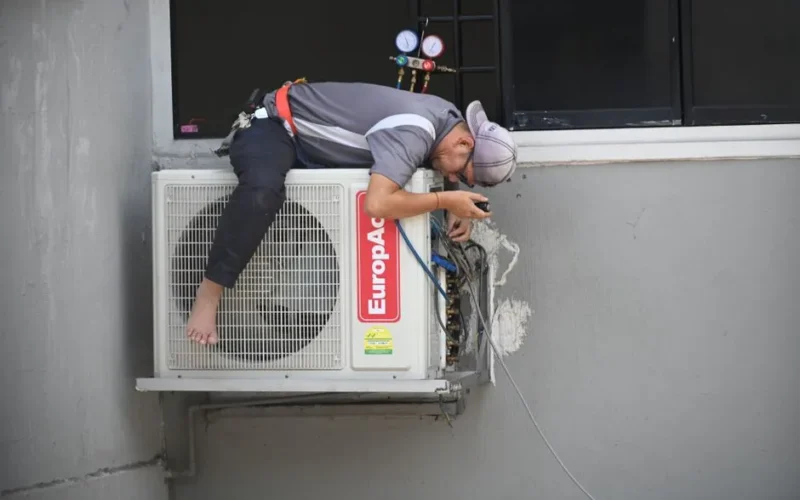 A technician skillfully repairing an outdoor air conditioning unit mounted on a building wall.