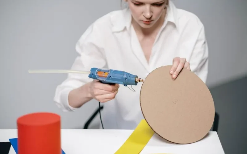 Young woman using a glue gun for a DIY cardboard project.