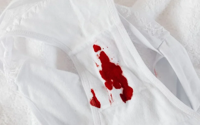 Close-up of white panties with red menstrual blood stain on white background.