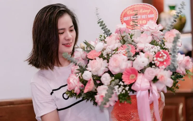 Young woman smiles while holding a vibrant floral bouquet inside. Perfect for celebrations.