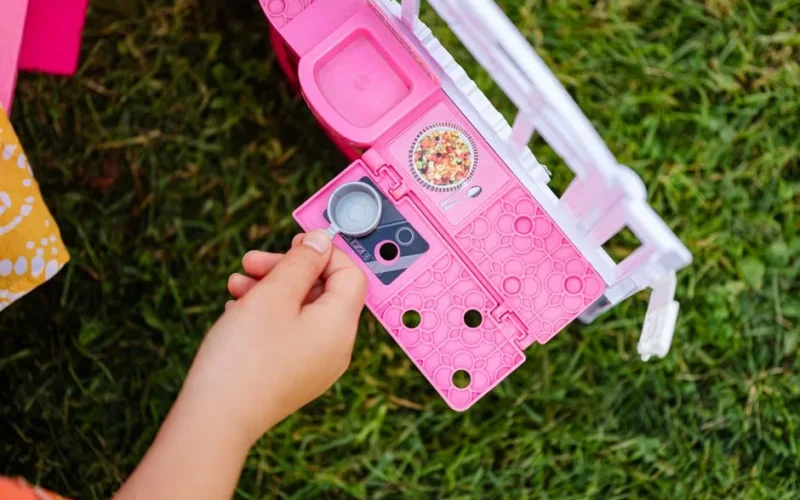 A child interacting with a pink toy kitchen set on green grass, showcasing playtime creativity.