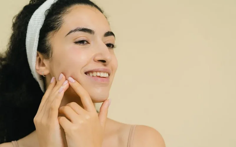 Close-up of a smiling woman applying skin treatment, promoting natural beauty and skincare.
