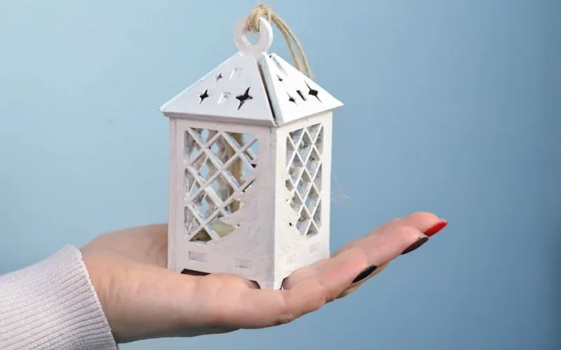 Close-up image of a white decorative lantern held in a hand, set against a solid background.
