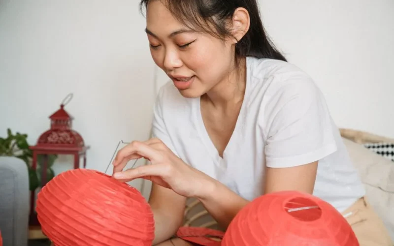 A young woman delicately assembling vibrant red paper lanterns indoors, capturing cultural tradition.