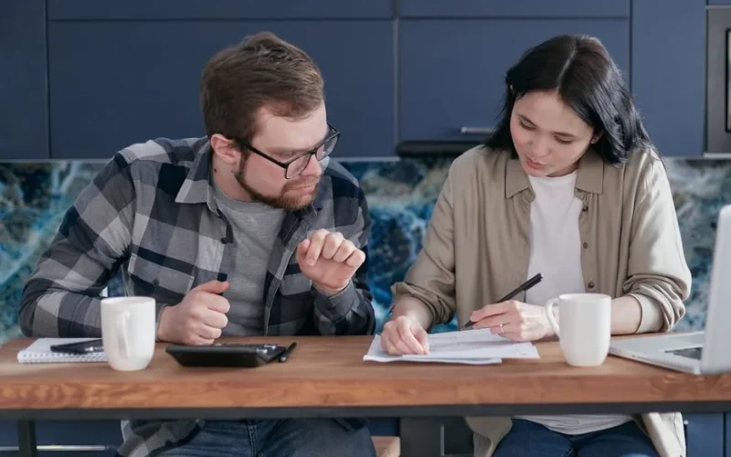 A couple sitting at a wooden table reviewing documents and discussing finances.