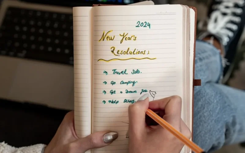 A person writes 2024 New Year's resolutions in a notebook. Concept of planning and personal goals.