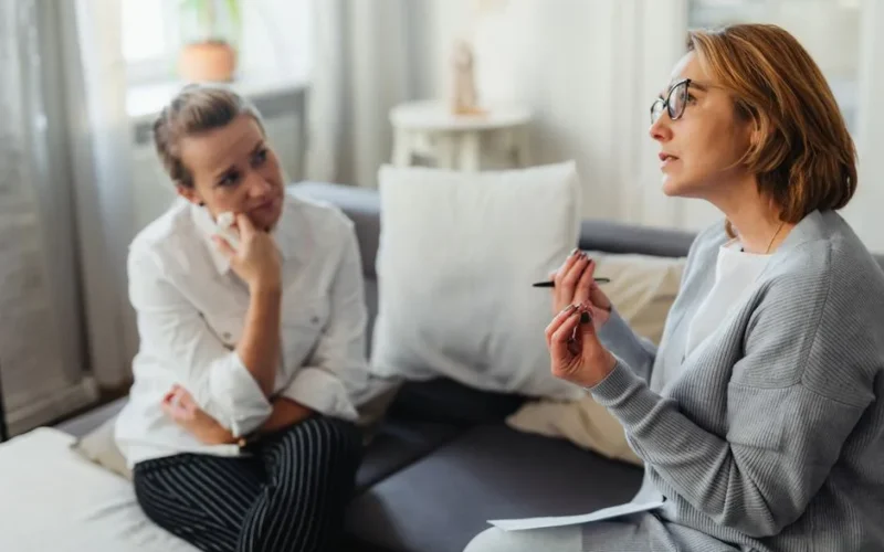 Two women engaged in a thoughtful counseling session in a cozy indoor setting.