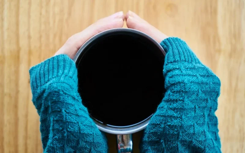 Close-up of hands holding a coffee cup, wrapped in a cozy teal sweater, perfect for a warm comfort theme.