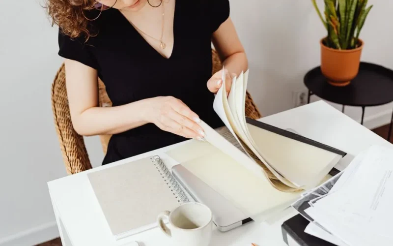 Woman at desk flipping through paperwork, workspace setting, organized.