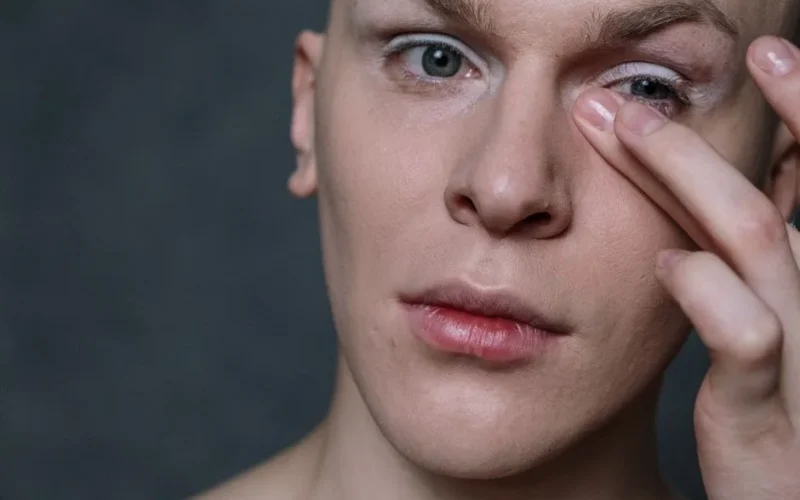 Portrait of a man applying makeup to his eyelid, showcasing a beauty routine.
