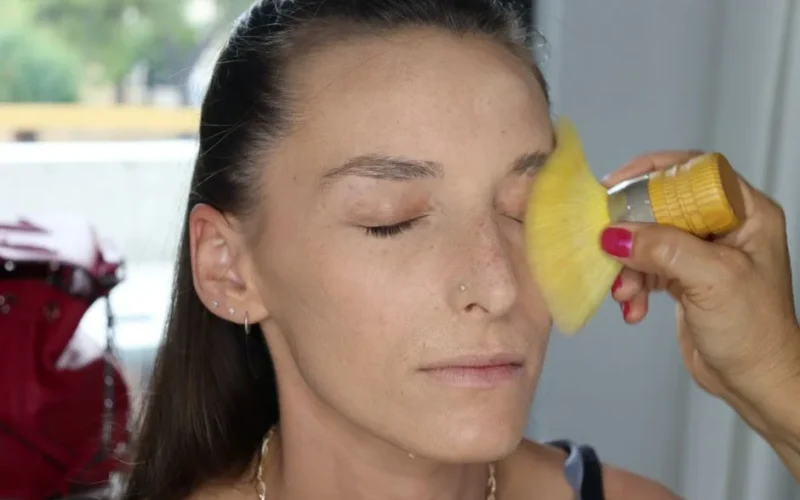 Close-up of a woman having makeup applied with a brush, emphasized focus on the face.