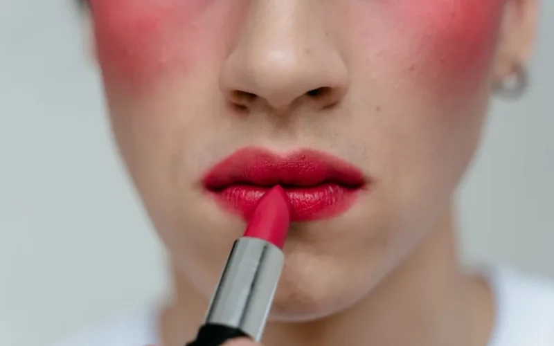 Close-up view of a person applying red lipstick to their lips, highlighting vibrant makeup.