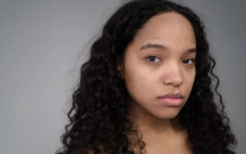 Close-up portrait of a young woman with curly hair and natural skin texture, looking confidently at the camera.