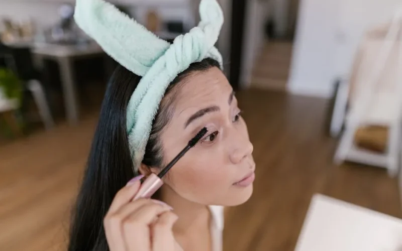 Asian woman applying mascara indoors for a natural beauty look.