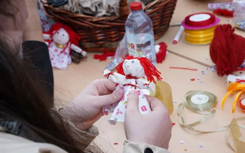 Person crafting a floral dress rag doll using colorful materials and threads.
