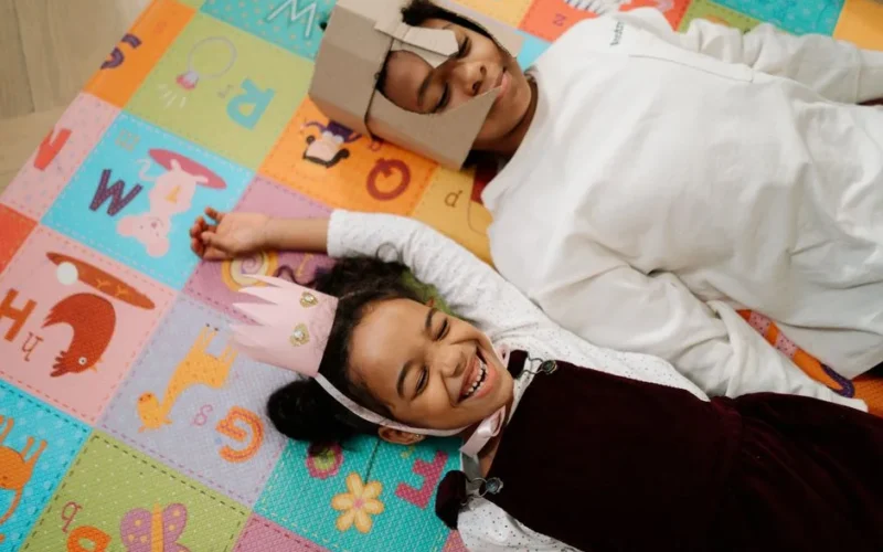 Two children having fun on a colorful play mat indoors, wearing creative DIY costumes.