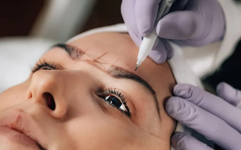 A beautician performs precise microblading on a client's eyebrows in a salon.