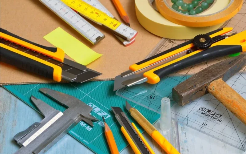 A variety of crafting tools including cutters, ruler, and tape on a work desk.